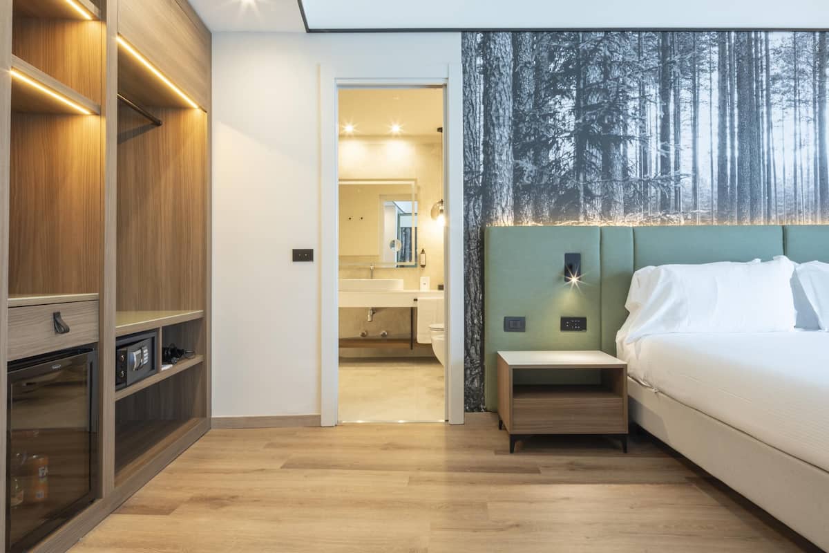 A modern bedroom with a wooden wardrobe, a nightstand, a bed, and a large forest-themed wall mural.
