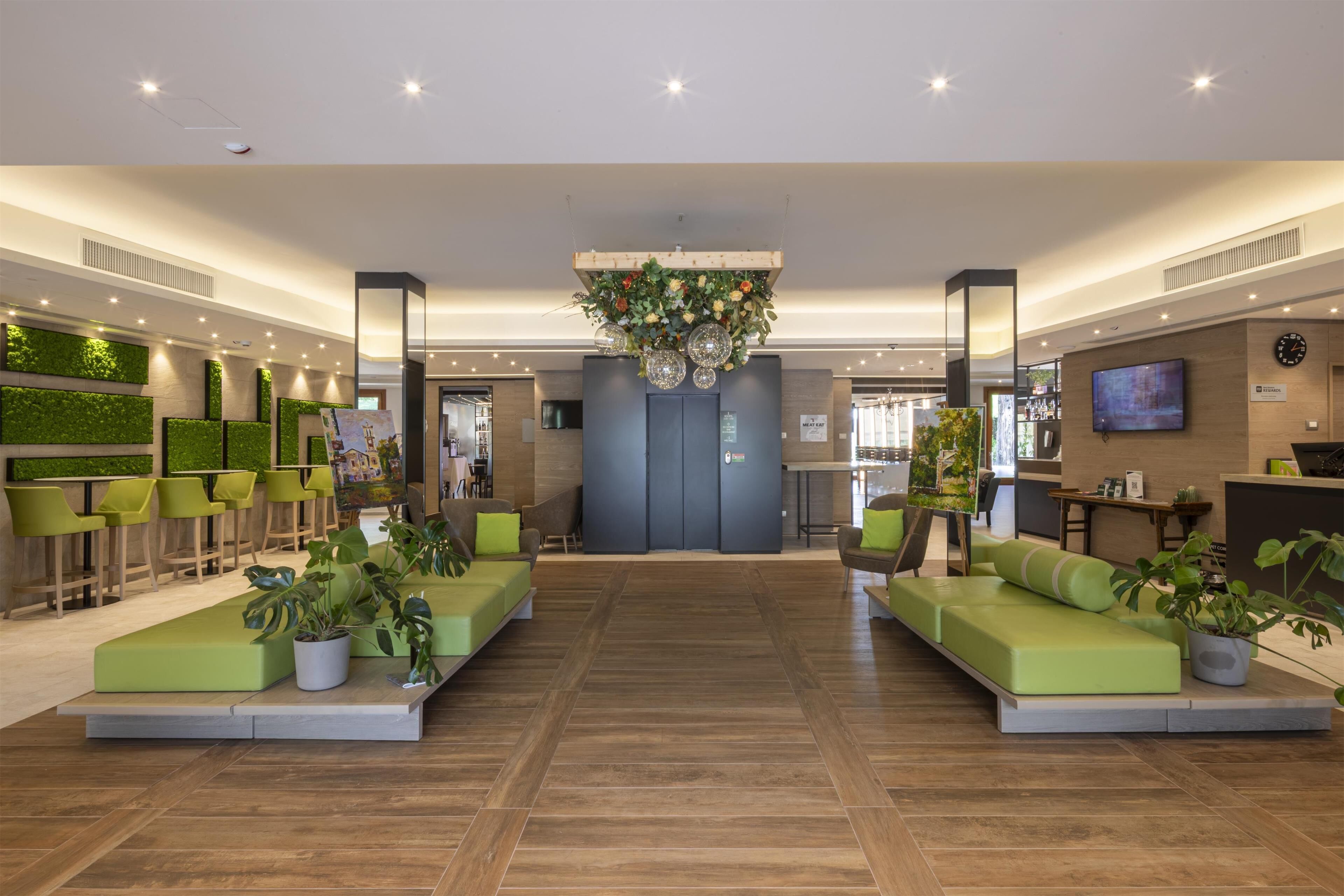 Un'ampia hall con zone salotto verdi, una reception e un grande schermo.