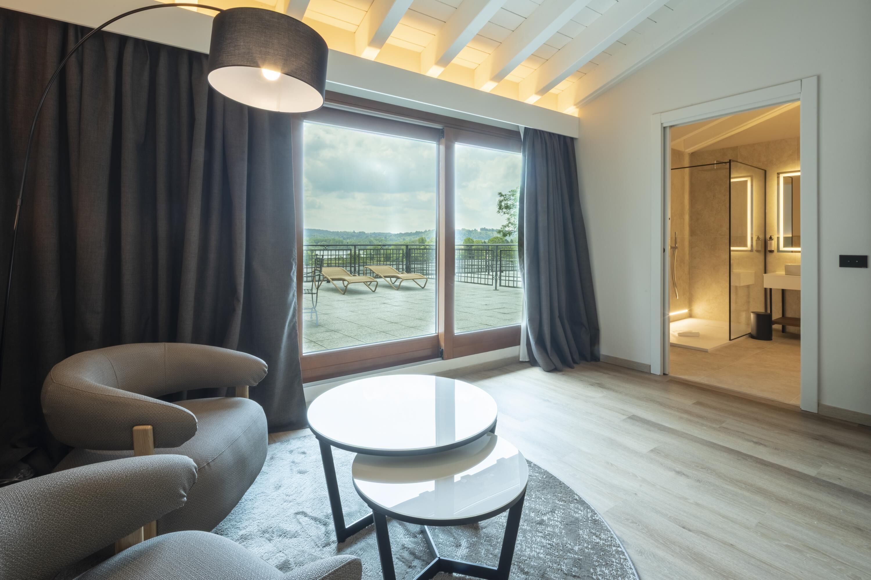 Una habitación moderna con sofá, una mesa redonda y un ventanal con vistas a un balcón y zona exterior.