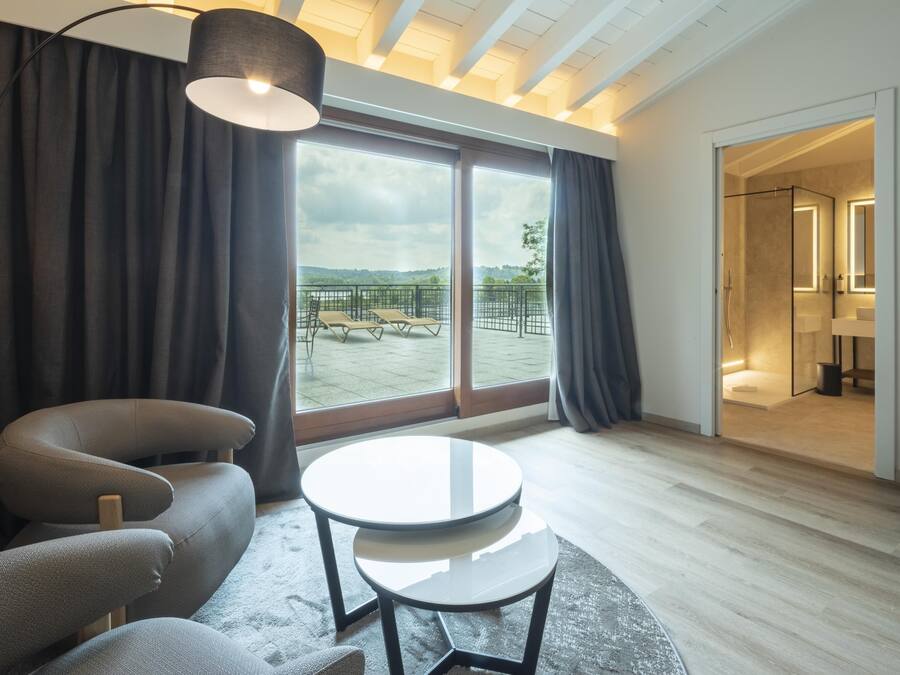 Een moderne kamer met een bank, een ronde tafel en een groot raam met uitzicht op een balkon en terras.