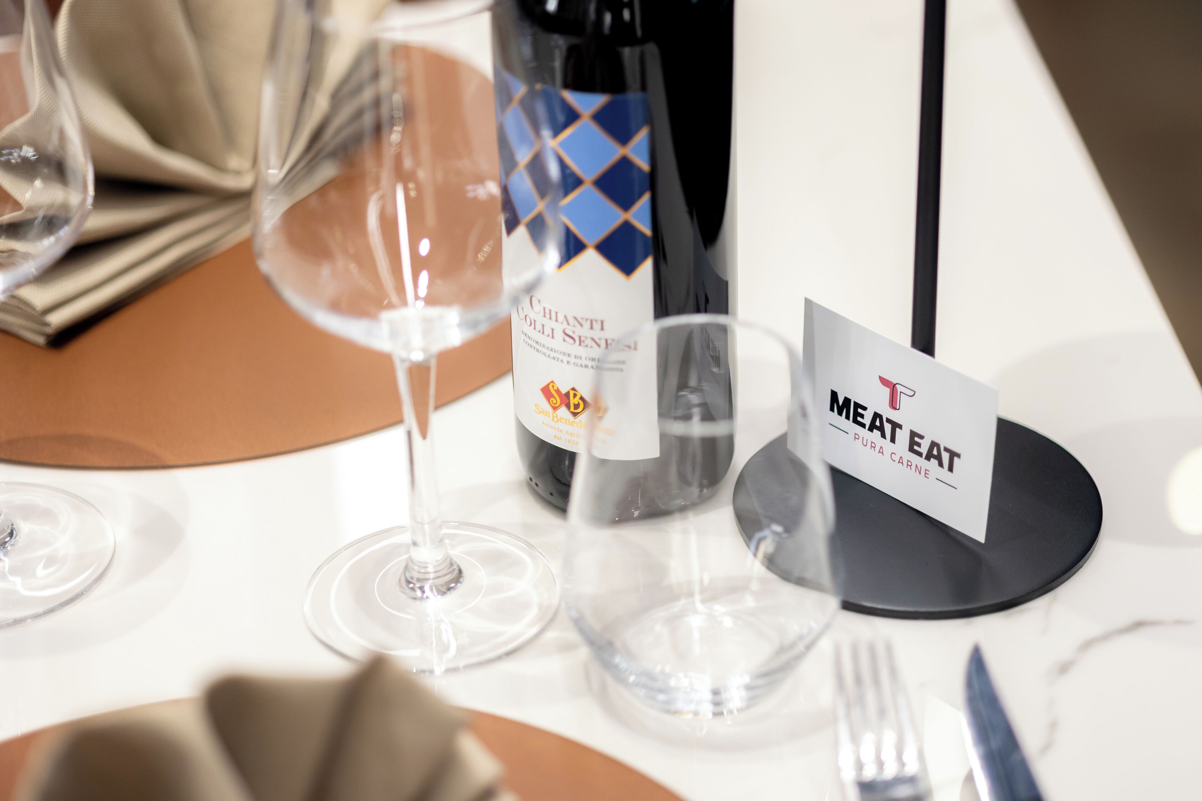A table set with wine glasses, a bottle of wine, a menu, and a sign indicating the meat section.