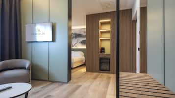 A modern hotel room with a bed, a TV, a sofa, and a small table.