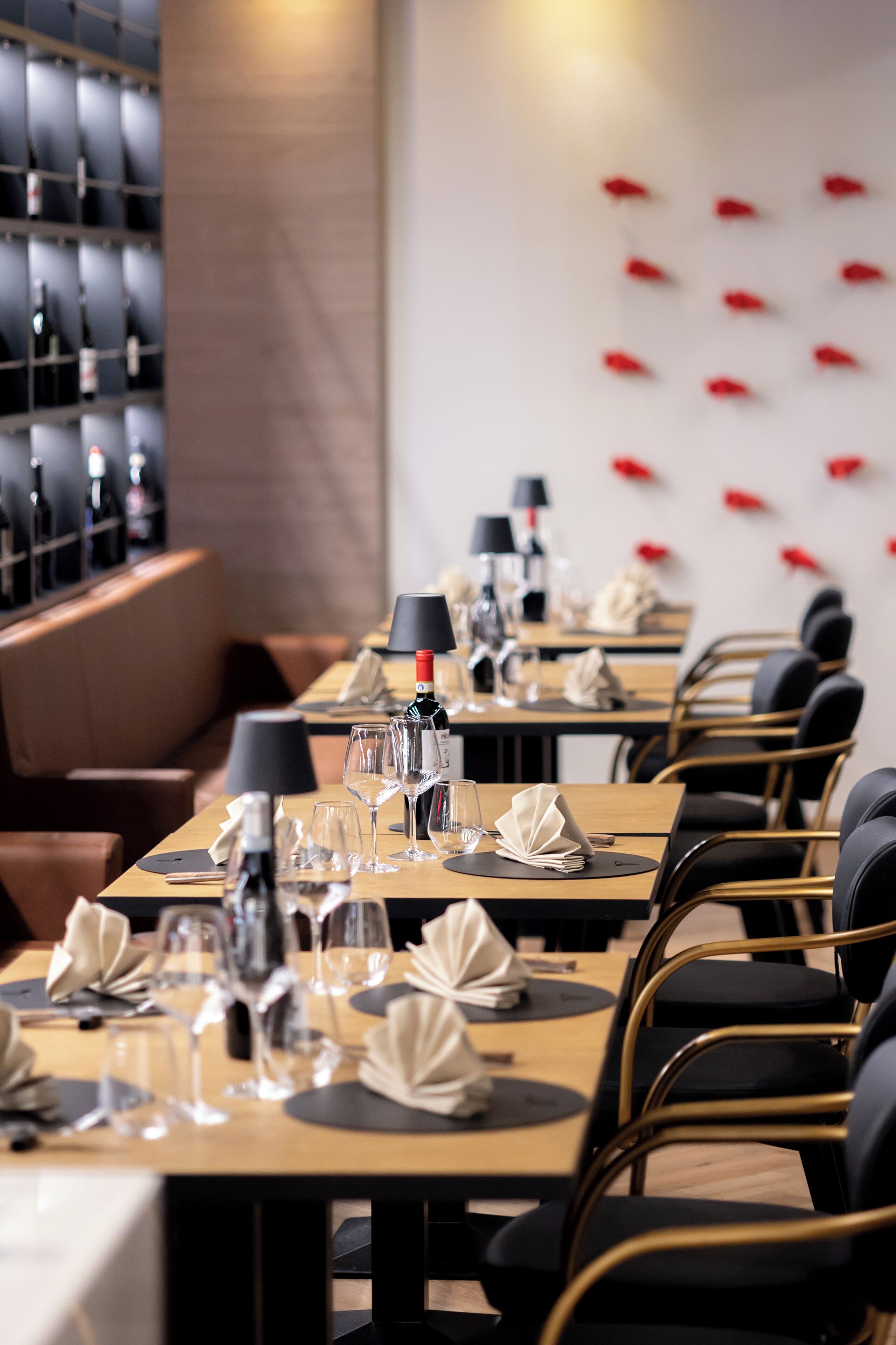 A restaurant with long tables set for dining, each with a bottle of wine, glasses, and folded napkins.