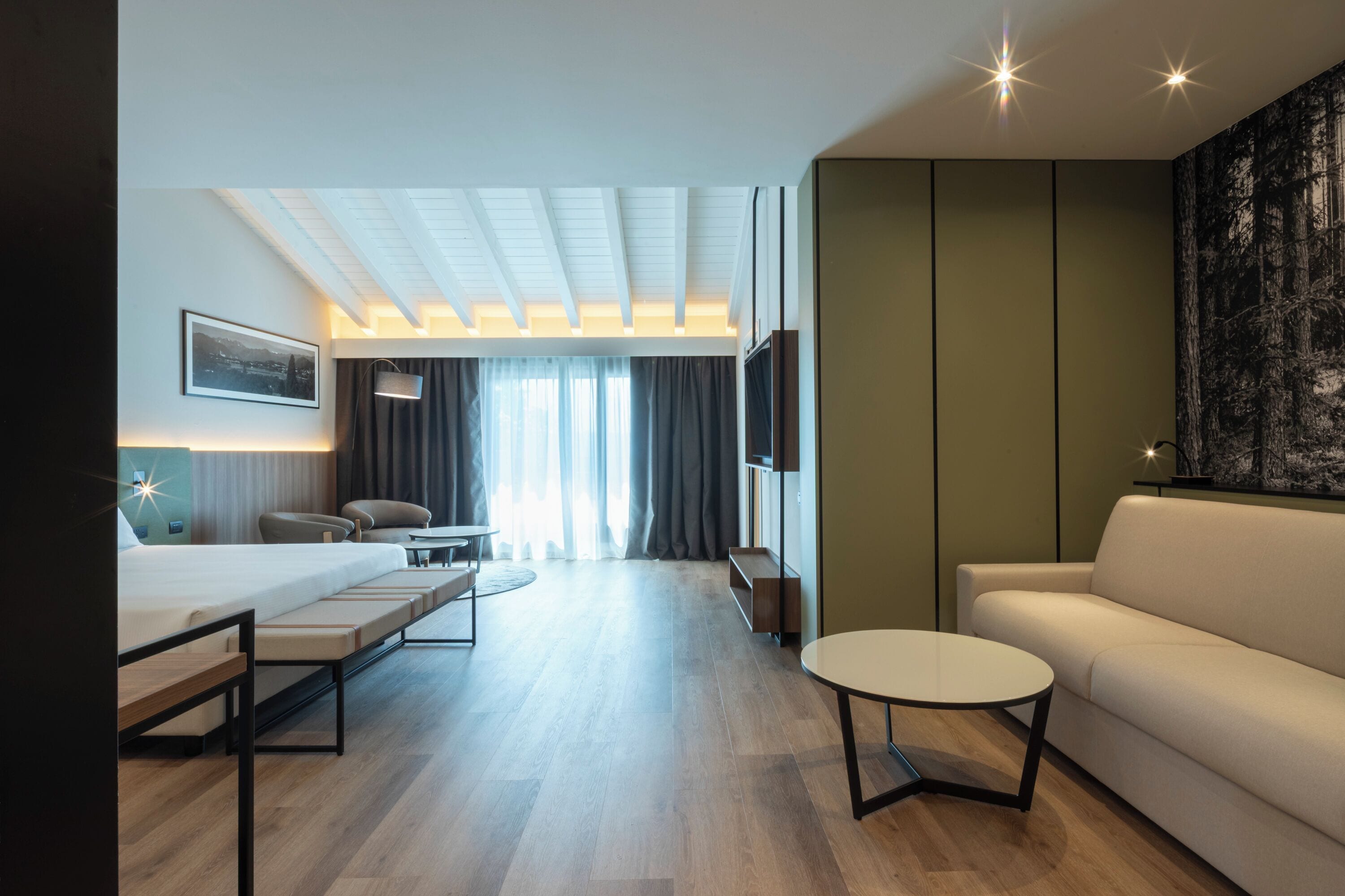 Ein modernes Hotelzimmer mit einem Bett, einer Couch, einem runden Couchtisch, einem Schreibtisch und einem Fernseher.