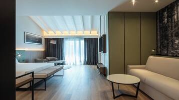 Ein modernes Hotelzimmer mit einem Bett, einer Couch, einem runden Couchtisch, einem Schreibtisch und einem Fernseher.