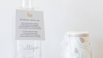 A clear glass bottle with a label and a clear glass mug with a design, both placed on a surface.