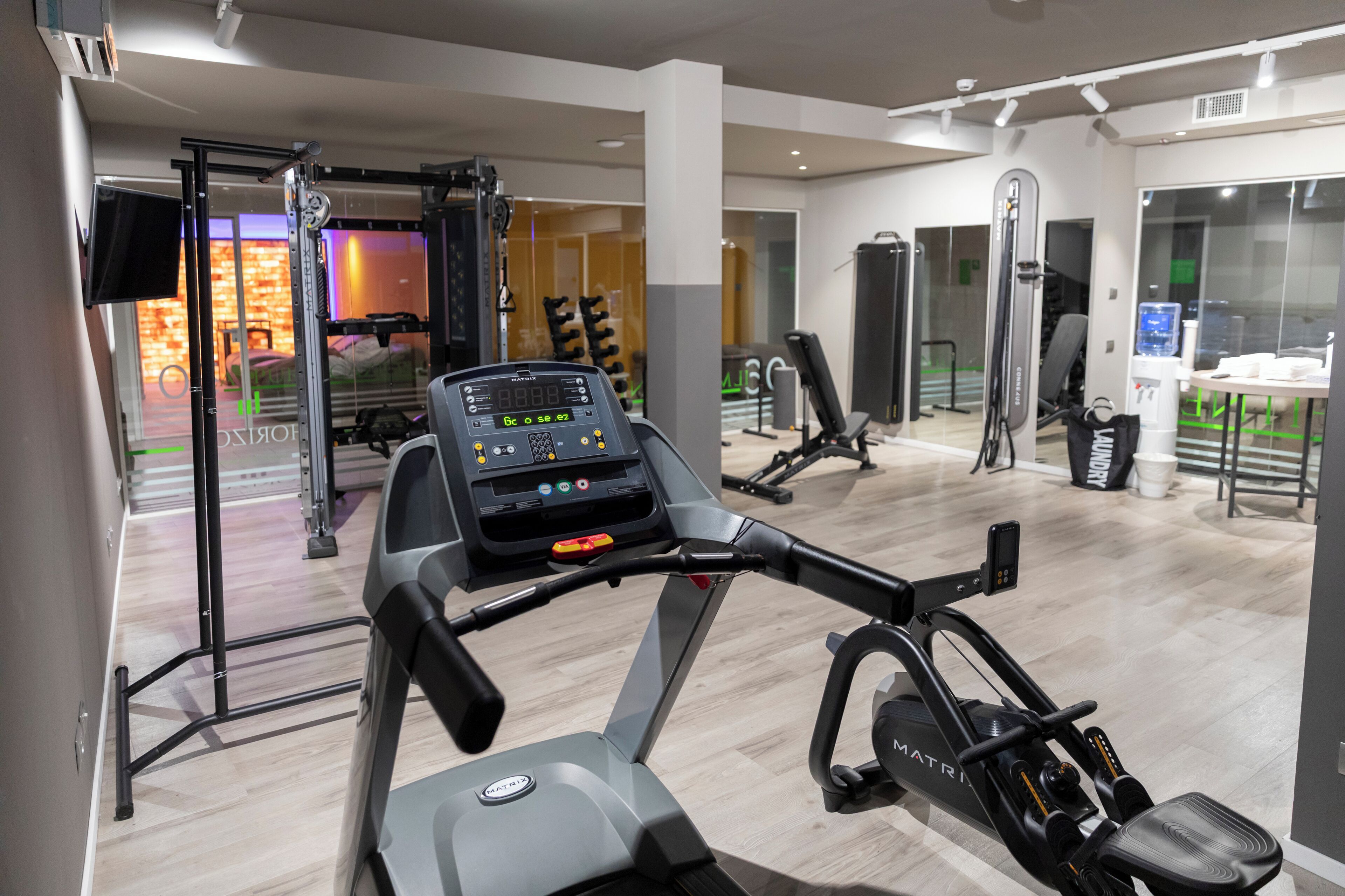 A modern gym with a stationary bike, weight machines, and a TV screen.
