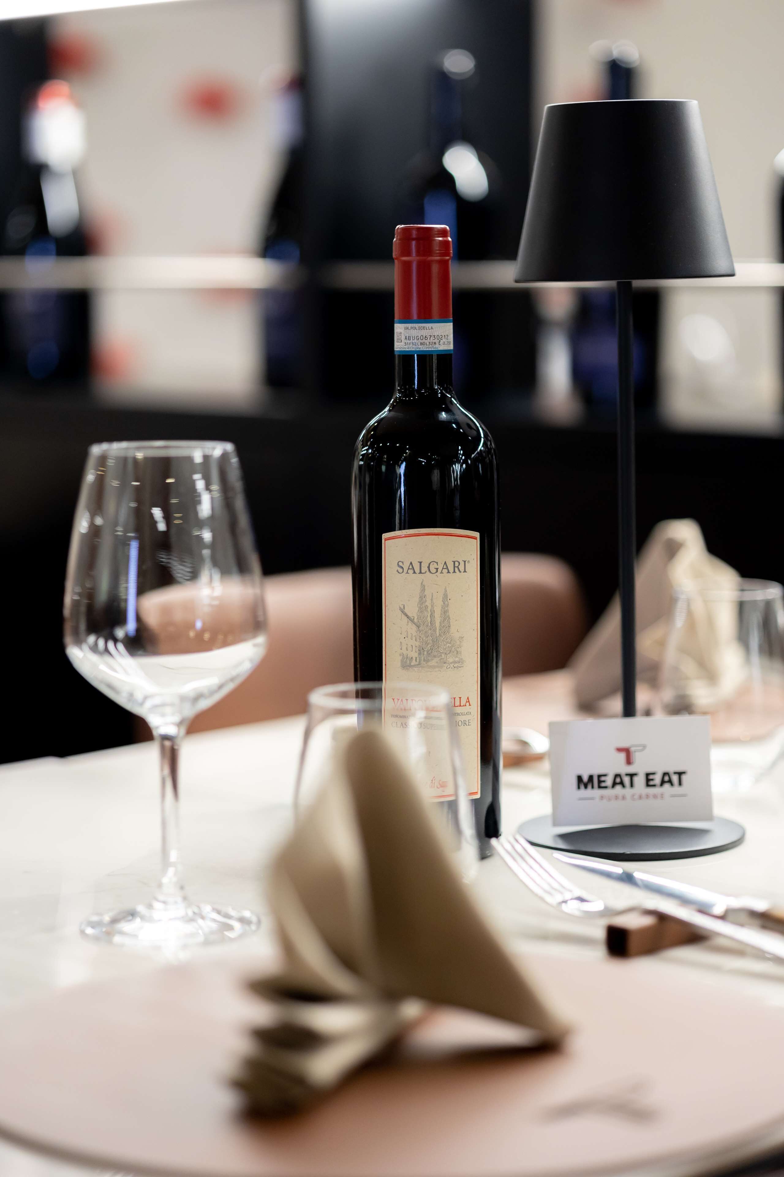 Una mesa de comedor con una botella de vino Salgari, una copa de vino y un letrero que indica una carnicería.