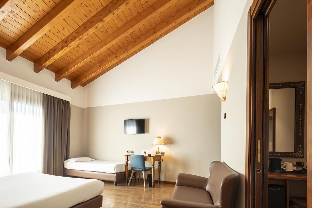 A hotel room with a wooden ceiling, a bed, a desk with a chair, a lamp, a television, and a mirror.