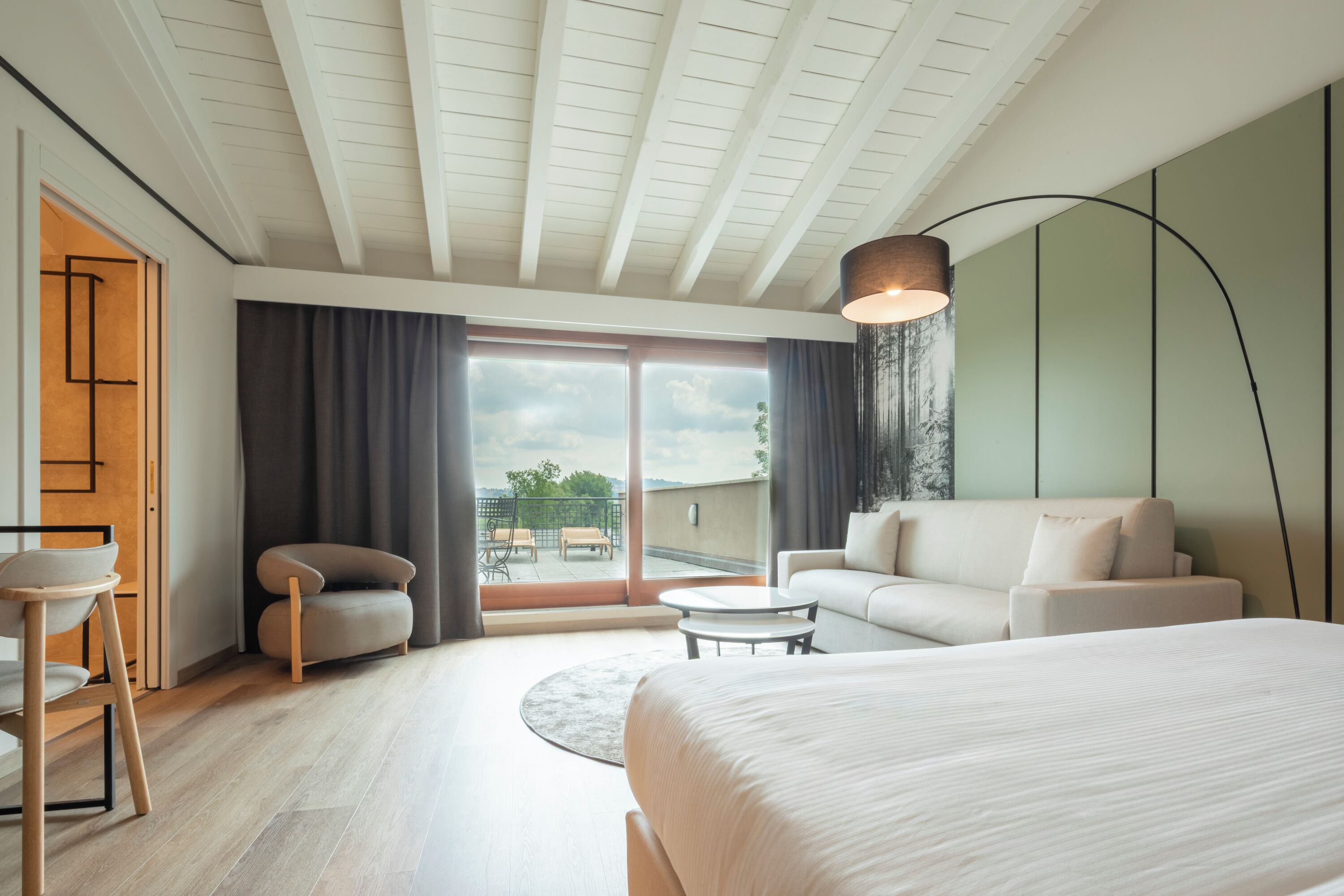 Habitación de hotel moderna con una cama grande, un sofá, una mesita y vistas al exterior.
