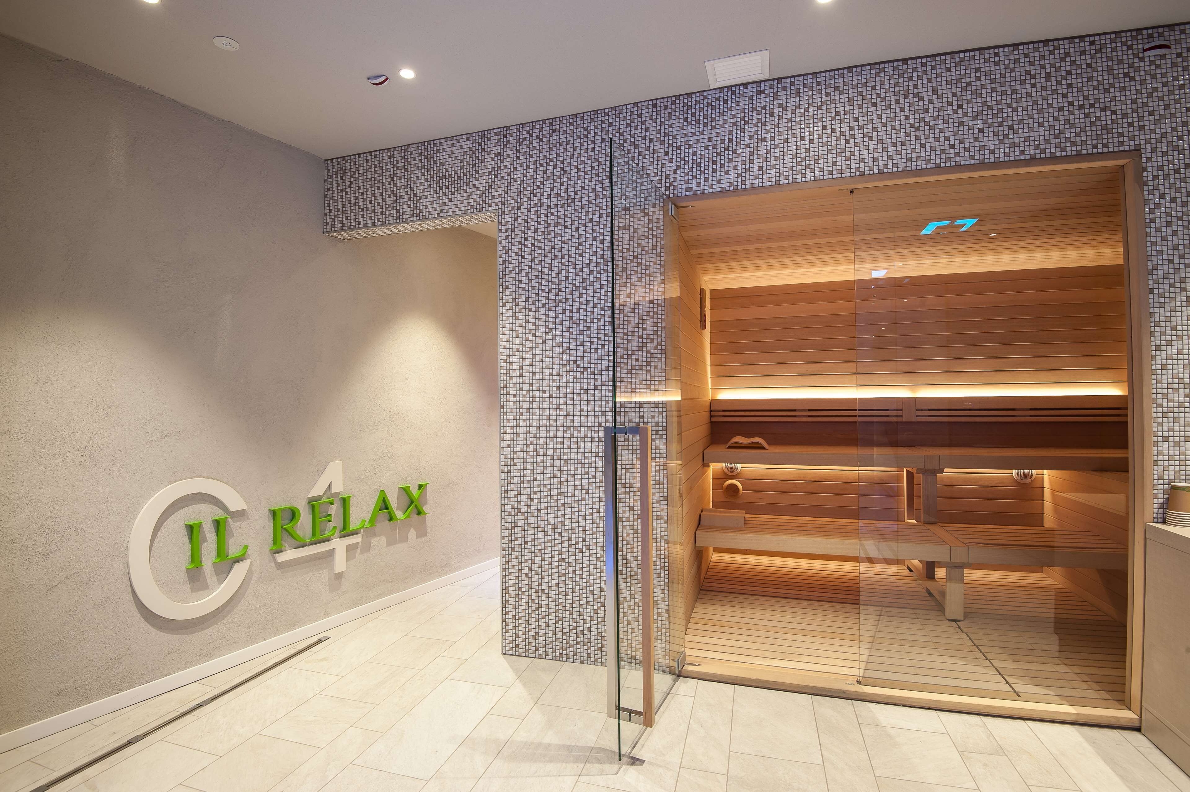 A modern spa entrance with a glass door, a wooden bench inside, and a tiled mosaic wall.