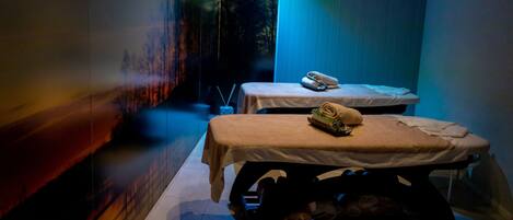 A dimly lit room with two massage tables, each with a towel and a small tray.