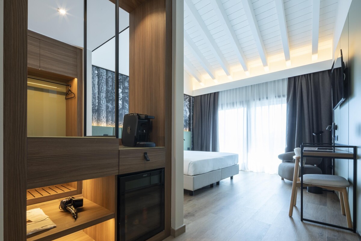A modern hotel room with a bed, a desk, a chair, and a built-in wardrobe.