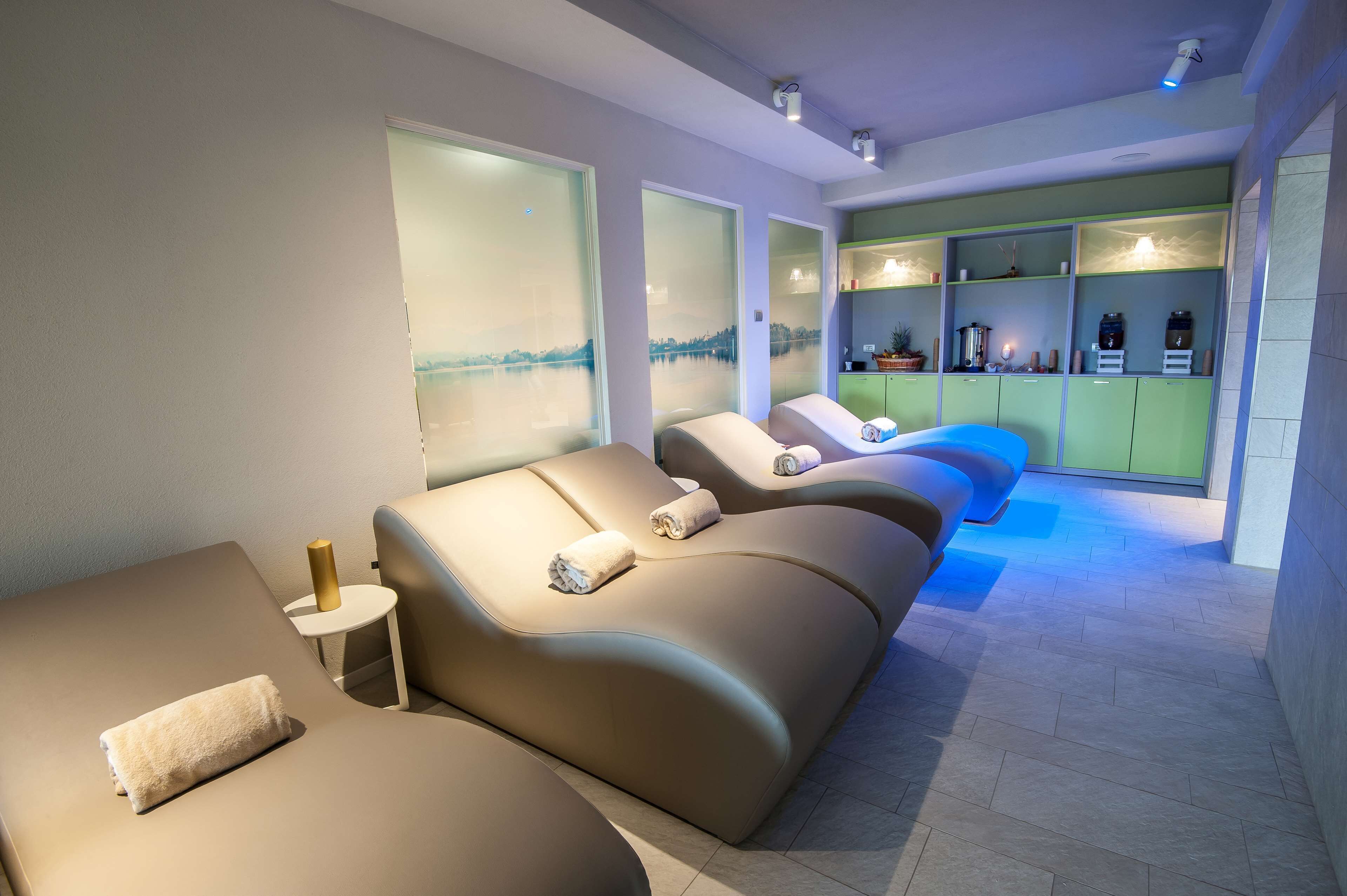 A spa room with three reclining massage chairs, a small table with a towel, and a shelf with various spa products.
