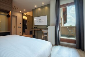 A hotel room with a bed, a desk, a chair, a TV, and a balcony with a view.