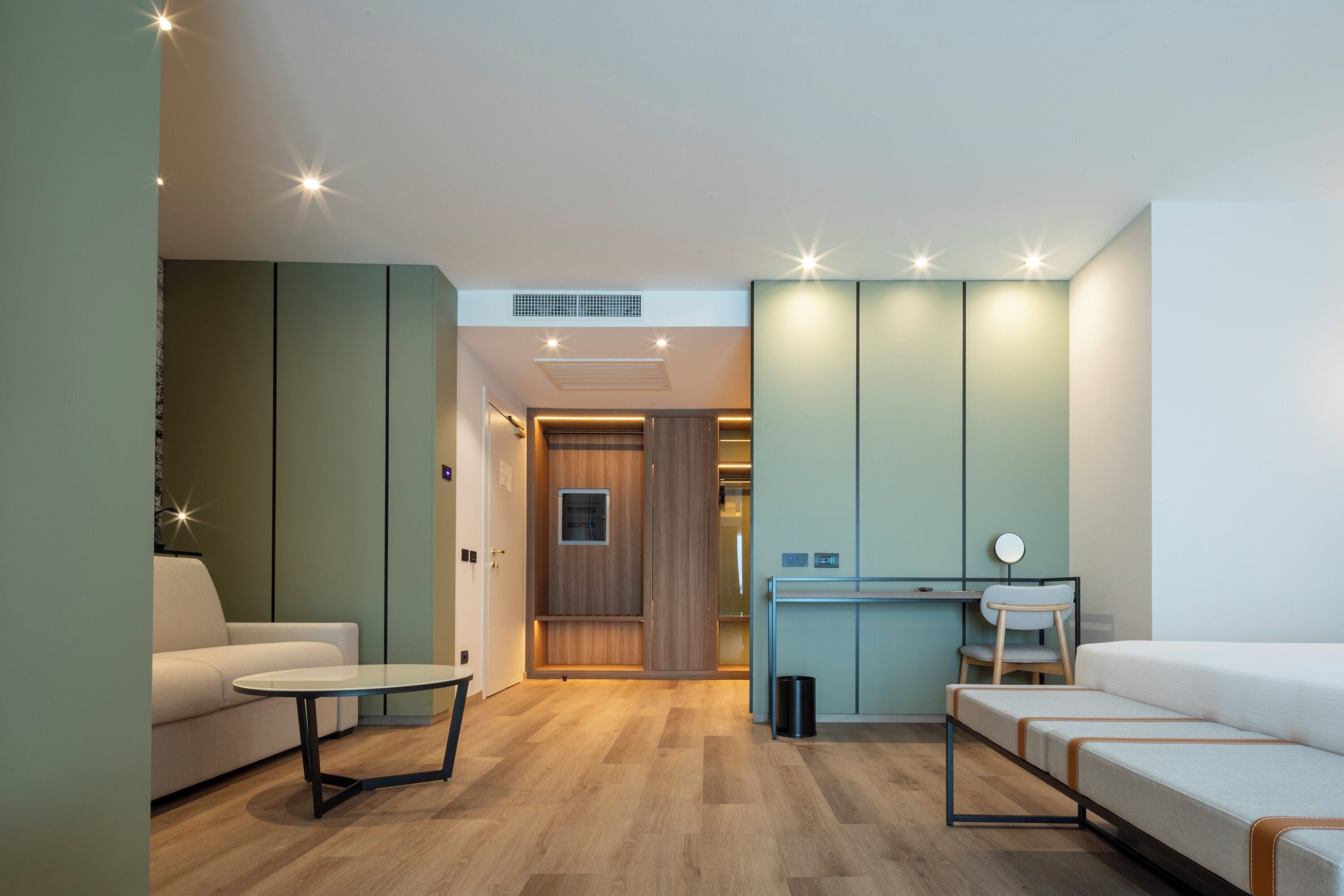 Een moderne woonkamer met een bank, een klein tafeltje, een bureau met stoel, en een bed.
