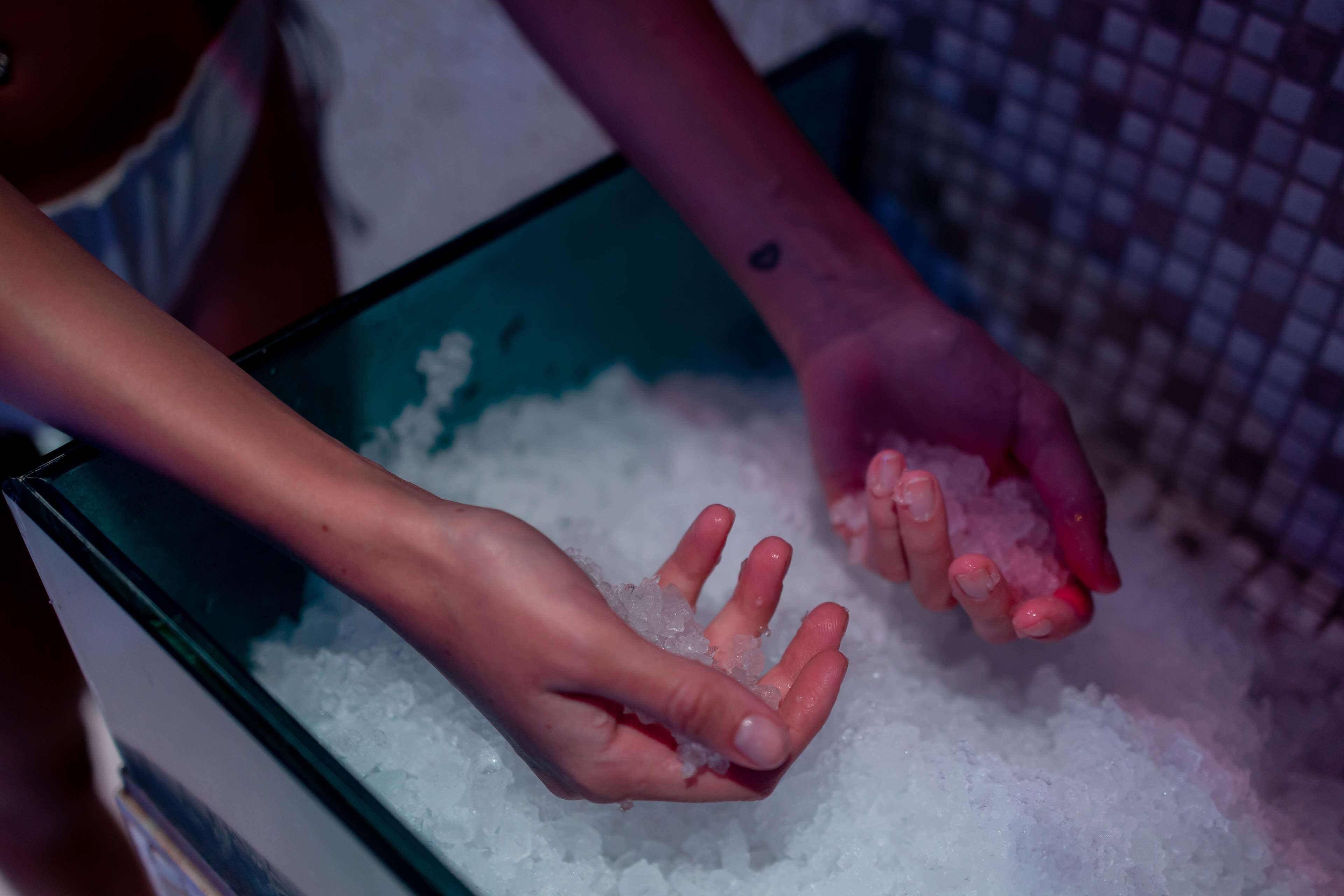 Hands holding ice cubes in a container.