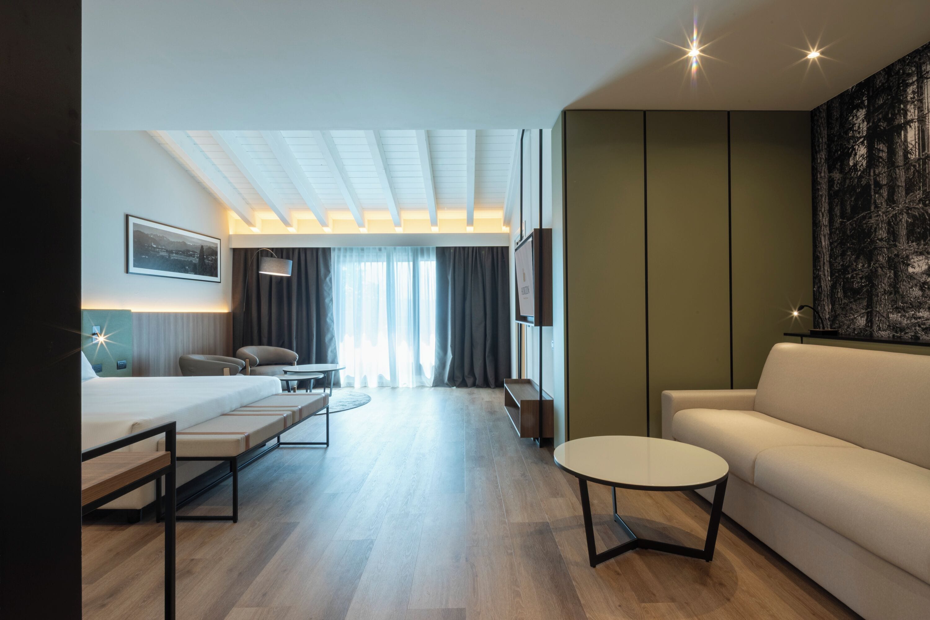 Ein modernes Hotelzimmer mit Bett, Sofa, rundem Tisch, Schreibtisch und Fernseher.