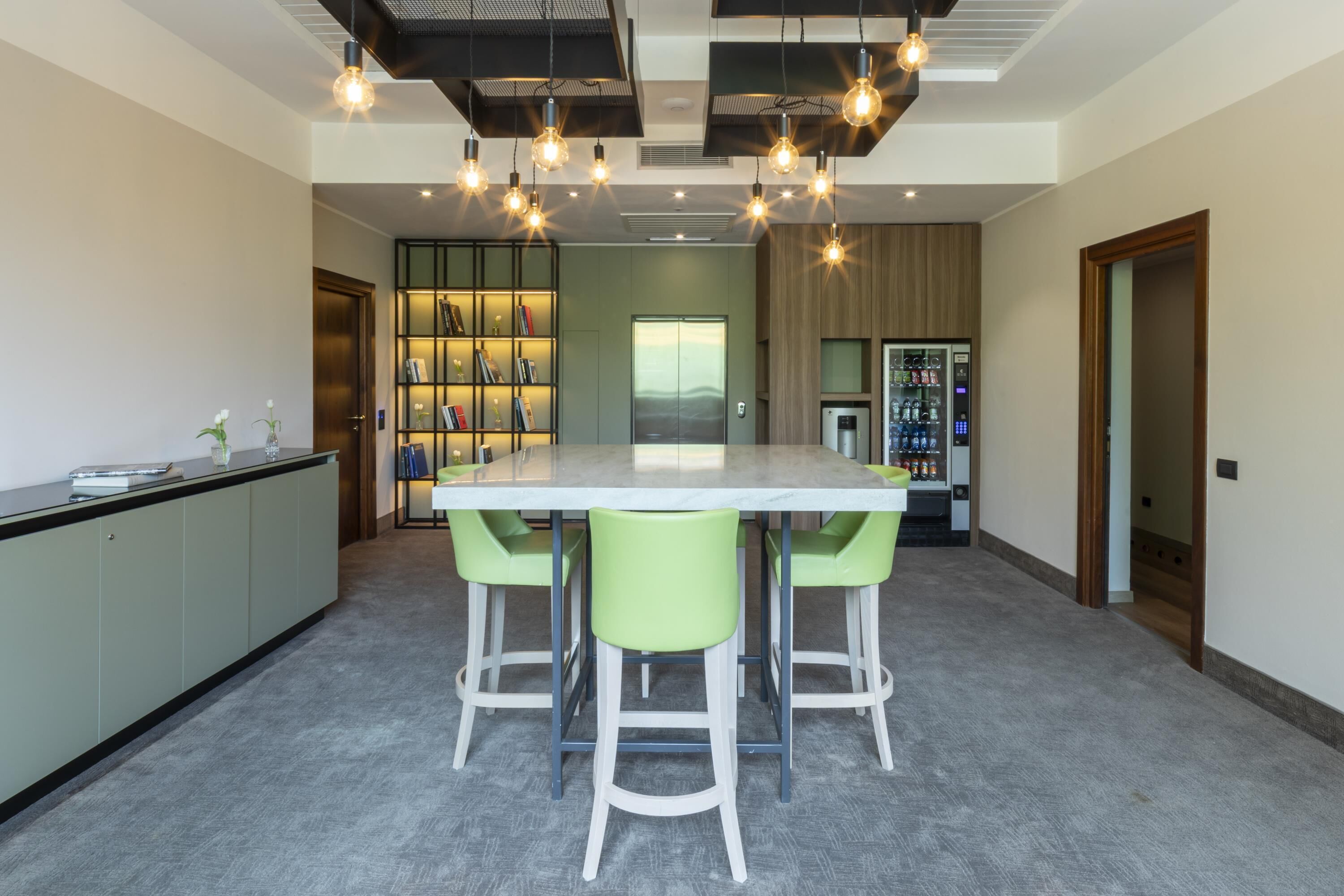 Une cuisine moderne dotée d’un plan de travail en marbre, de tabourets de bar verts, d’une bibliothèque intégrée et d’un distributeur automatique.