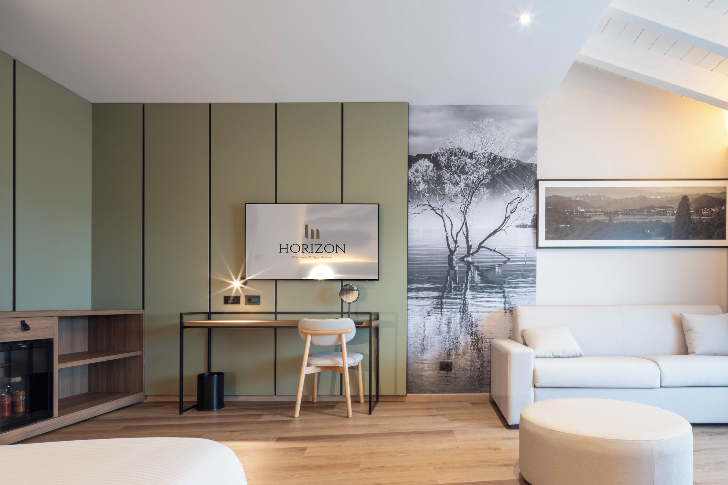 Una sala de estar moderna con un escritorio, un sofá blanco, un reposapiés redondo y un mural grande en la pared.