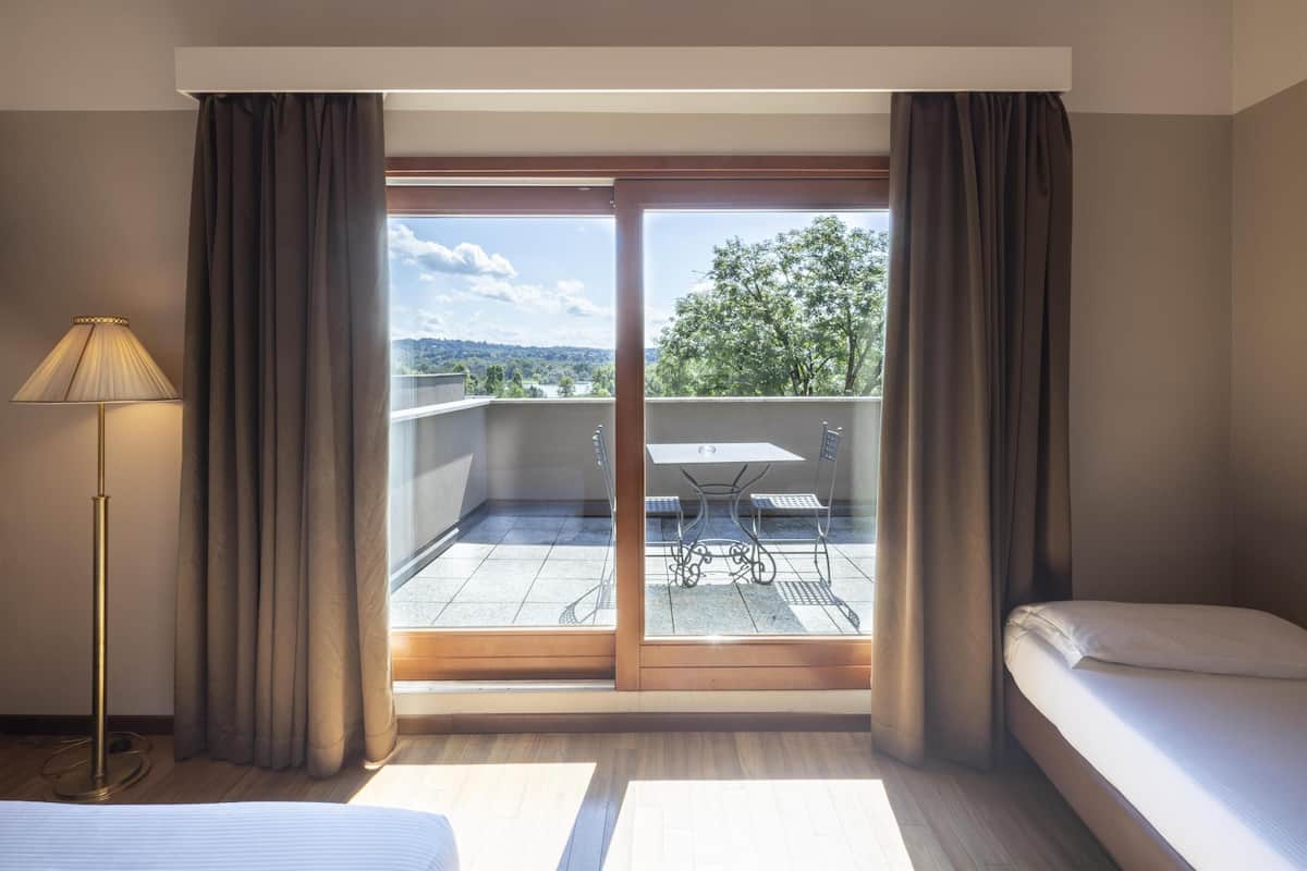 A hotel room with a bed, a desk, and a view of a balcony with a table and chairs.