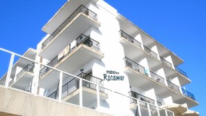 A multi-story hotel with balconies, a clear sky, and the name "Hotel Rocaminar" visible on the facade. - Hotel Rocamar (Santanyi)