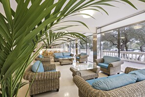 A spacious indoor seating area with wicker furniture and blue cushions, large windows offering a view of the outdoors. - Azuline Hotel Bahamas y Bahamas II (Llucmajor)