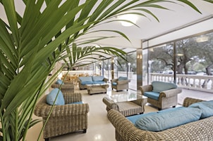 A spacious indoor seating area with wicker furniture and blue cushions, large windows offering a view of the outdoors.
