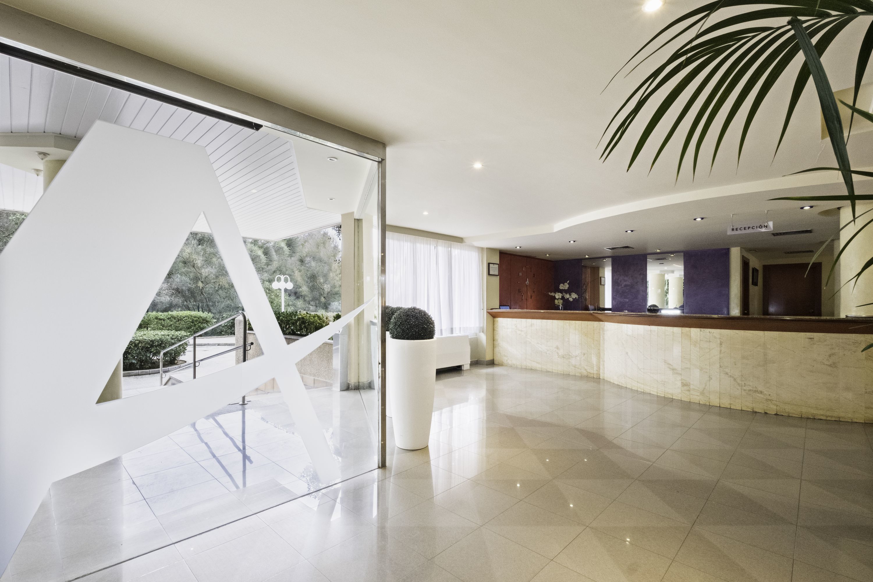 A modern hotel lobby with a reception desk, a large white abstract sculpture, and a potted plant.
