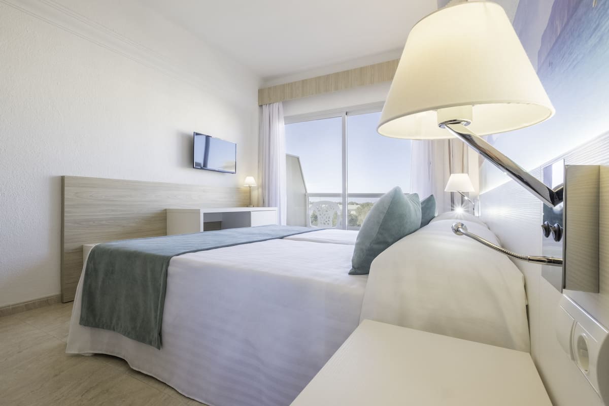 Habitación de hotel moderna con una cama grande, una mesita de noche, un televisor y una ventana con vistas.