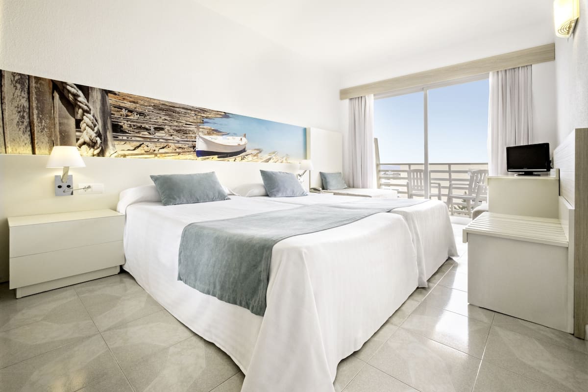 Habitación de hotel con una cama grande, televisión, escritorio y balcón con vistas.