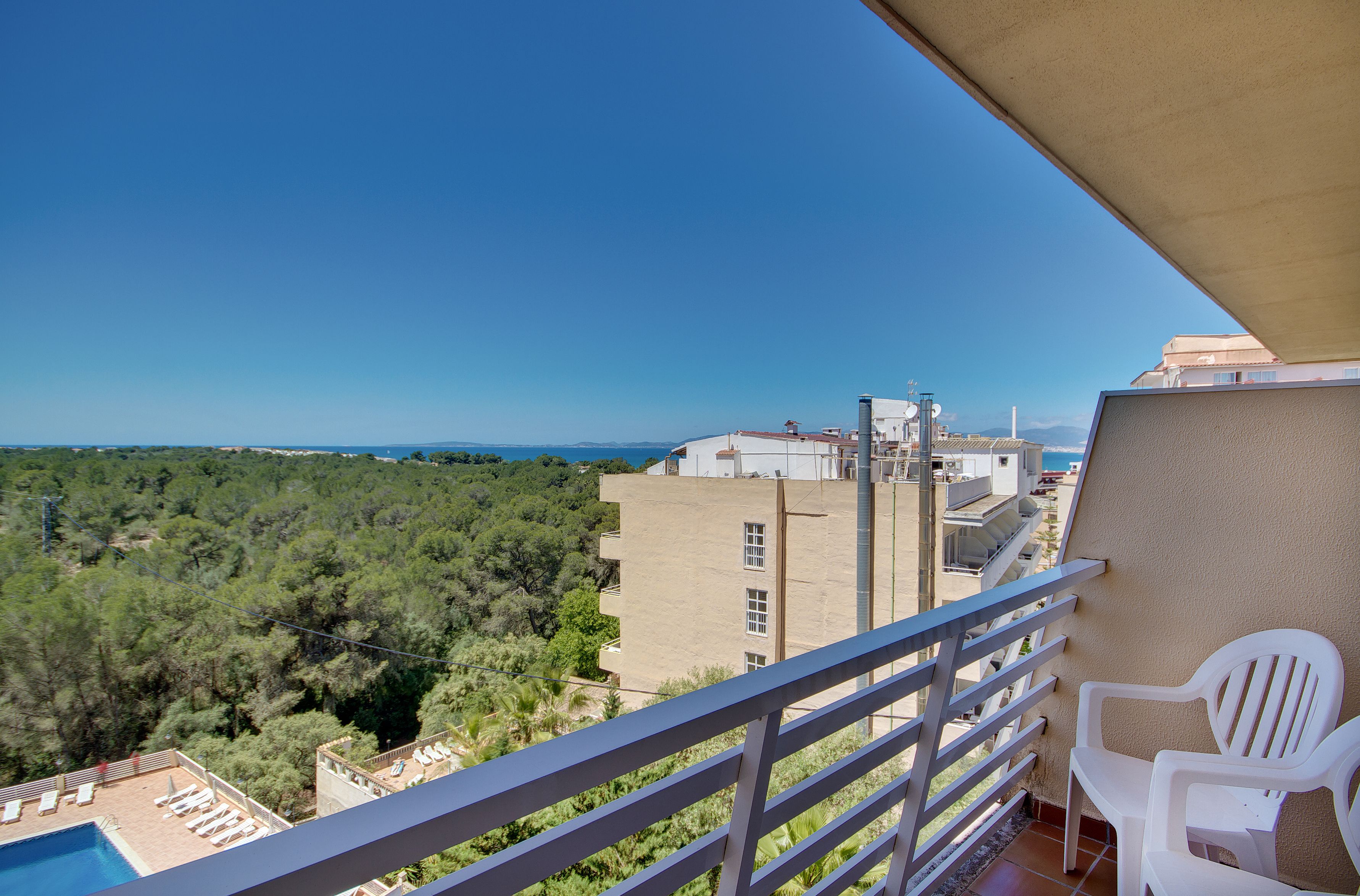 A balcony with a view of a swimming pool, trees, and buildings.
