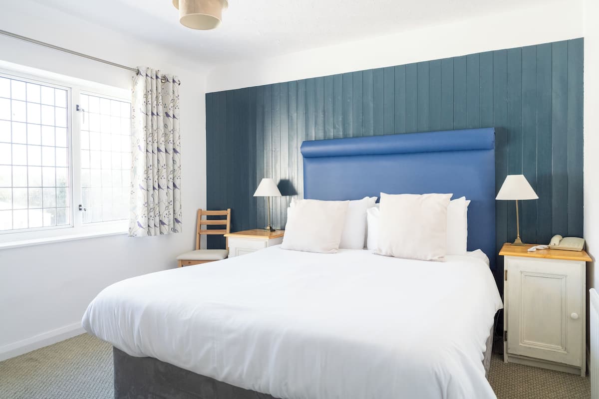 A bedroom with a large bed, two bedside tables, a chair, and a window with curtains.