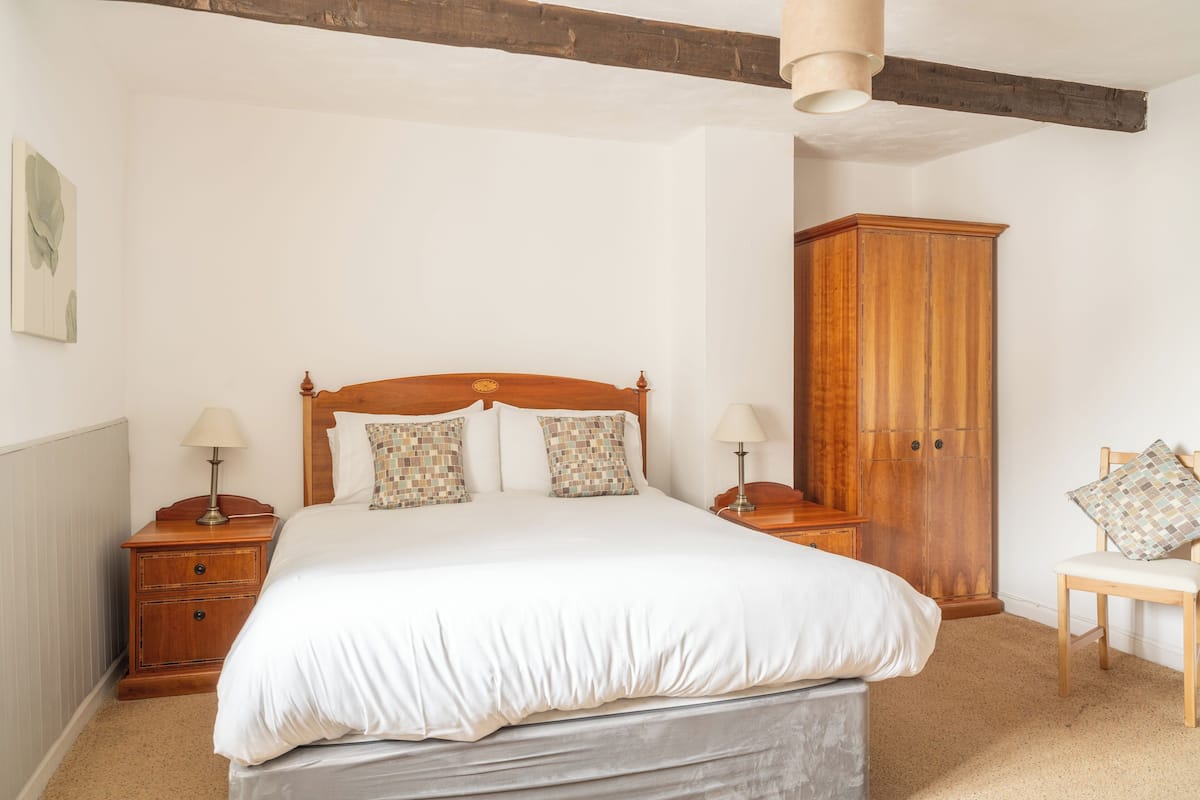 A bedroom with a wooden bed, two bedside tables with lamps, a wooden wardrobe, and a chair.