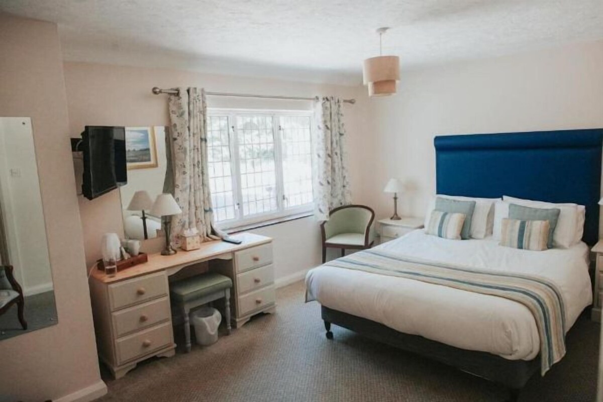 A bedroom with a bed, bedside table, lamp, and a window with curtains.