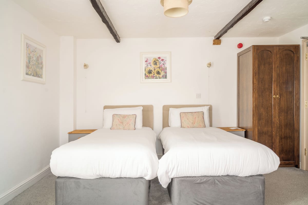 A room with two single beds, a wooden wardrobe, and a framed floral artwork on the wall.