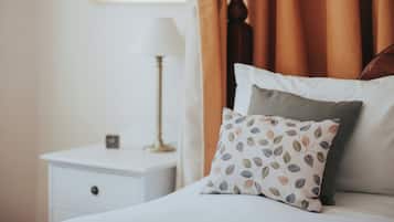 A neatly made bed with a patterned pillow and a plain pillow, a bedside lamp, and a small clock on a white nightstand.