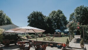 Eine Terrasse im Freien mit Holztischen und -stühlen, einem großen Sonnenschirm und Kübelpflanzen.