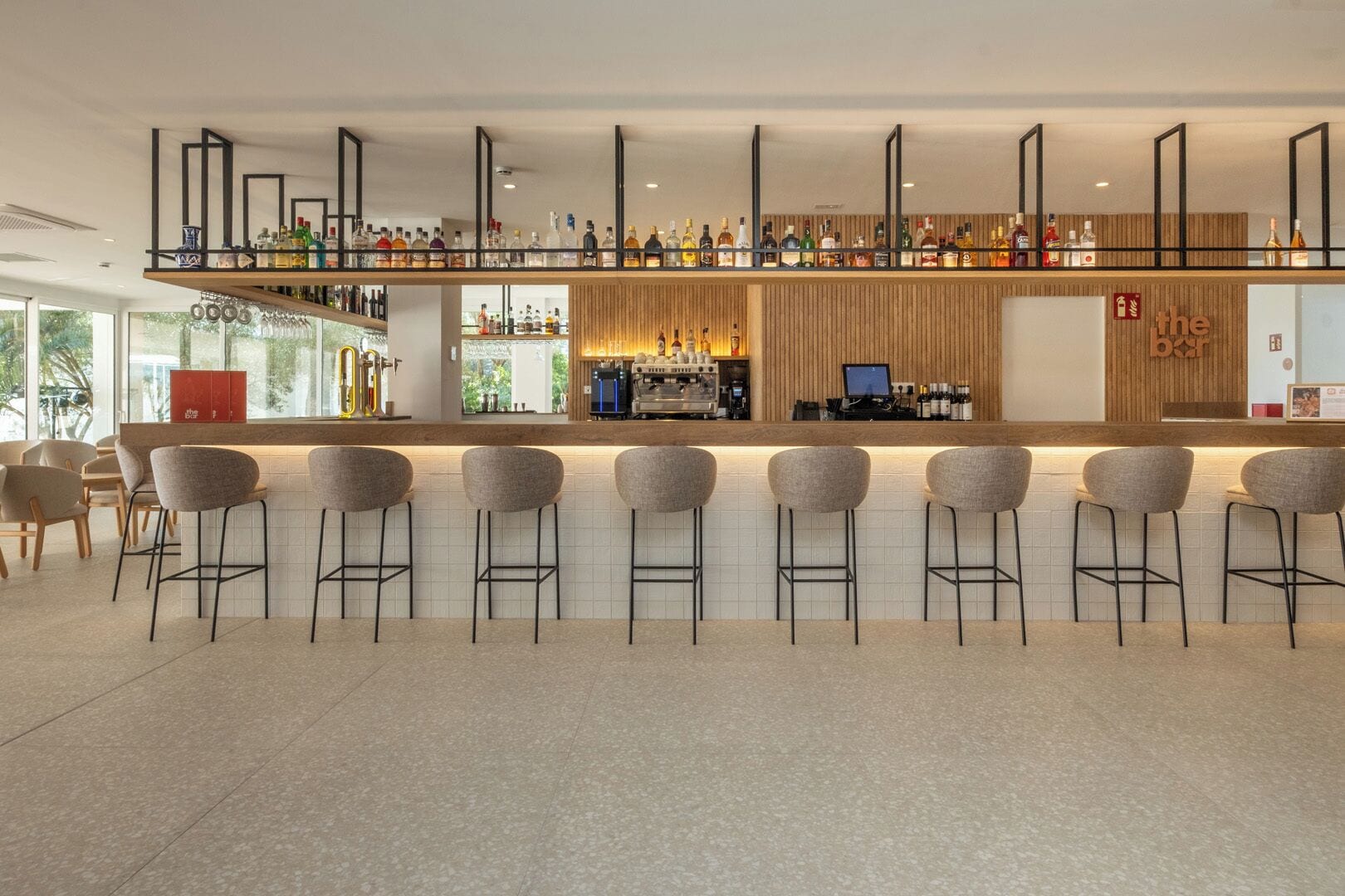 A modern bar area with a long counter, multiple stools, and a variety of bottles.