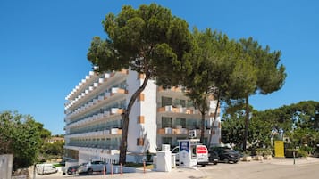 A multi-story hotel with an ATM on the ground floor, surrounded by trees and parked cars.