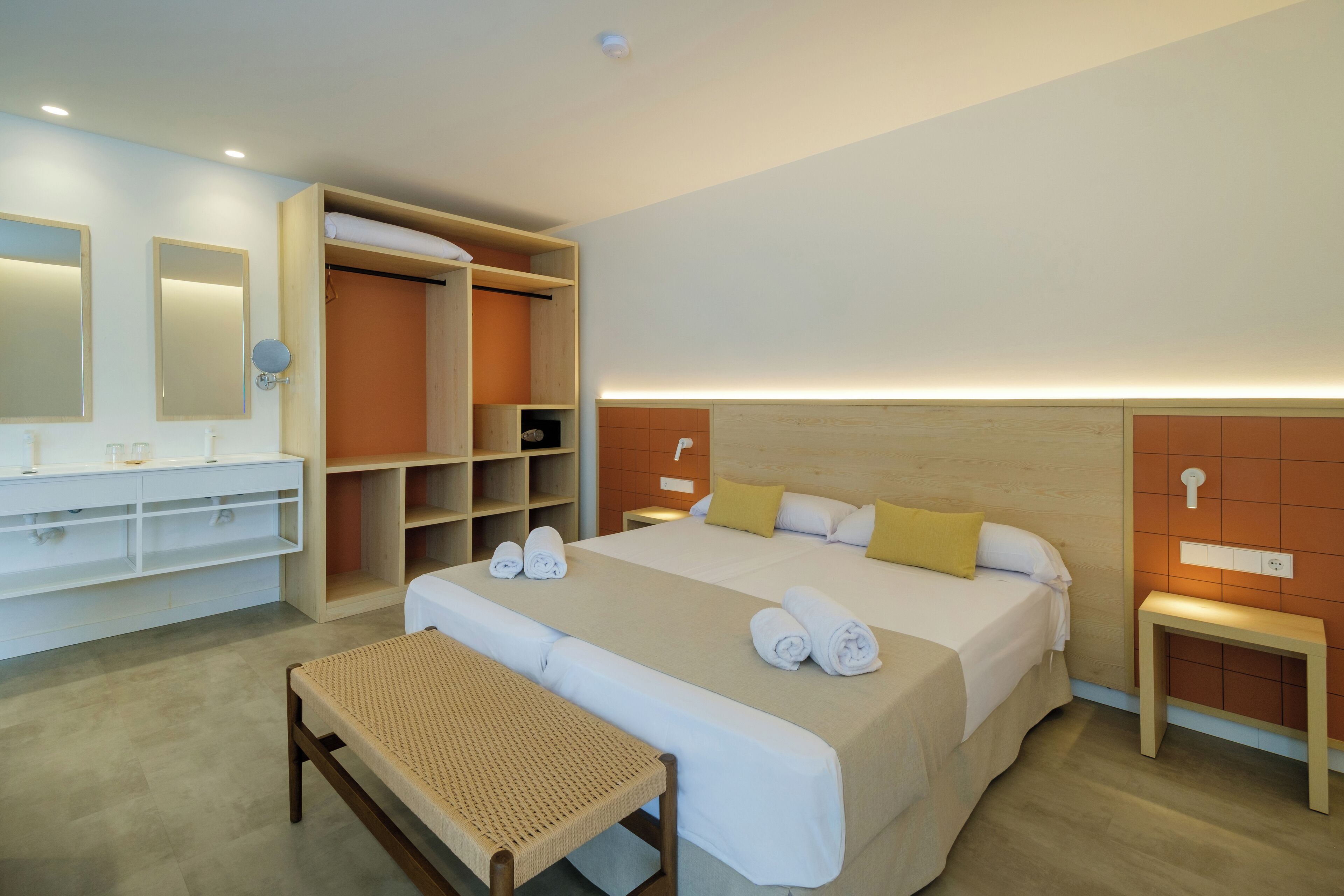 A modern hotel room with a large bed, a built-in wardrobe, a vanity with a mirror, and a bedside table.
