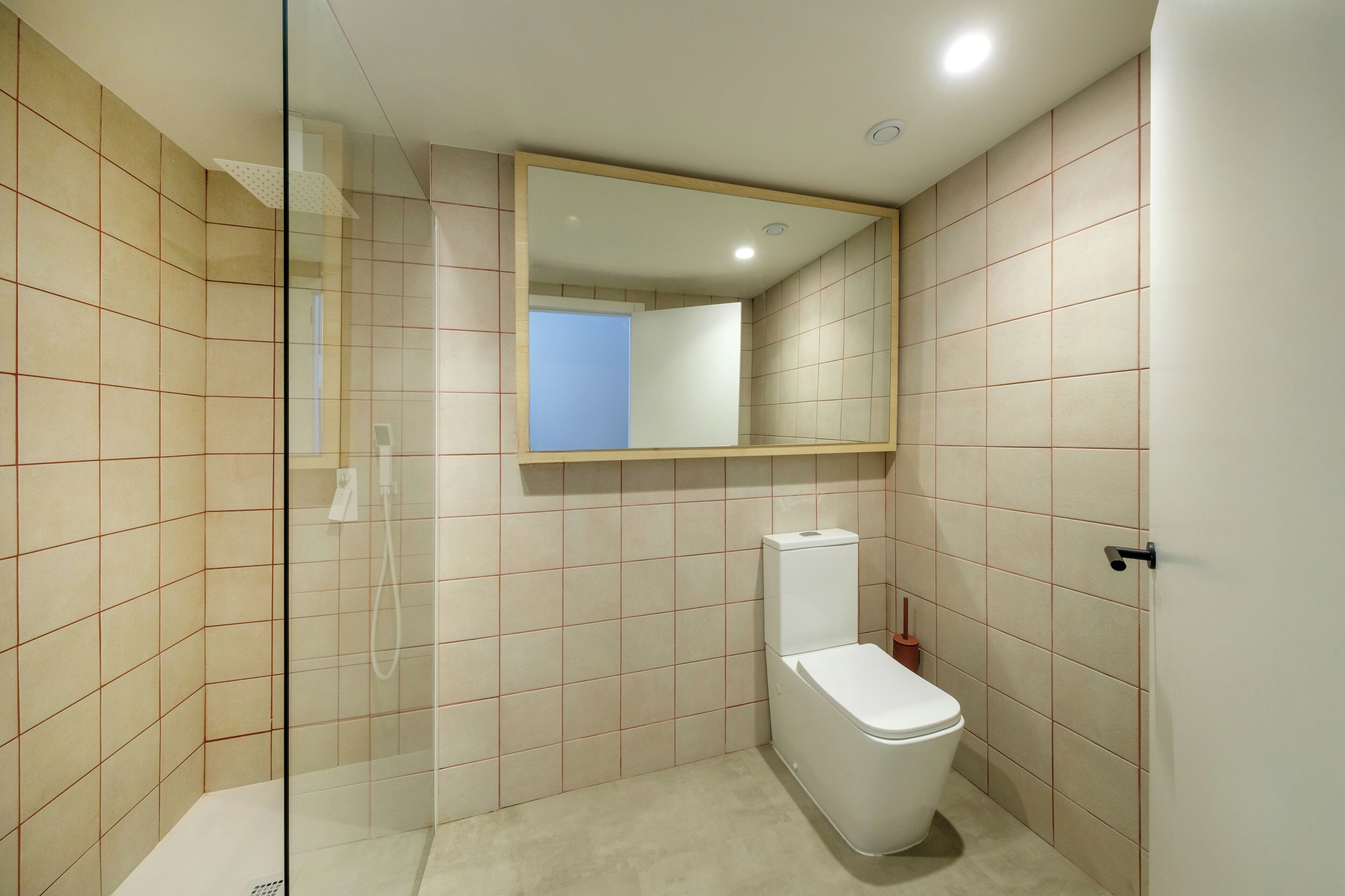 Un baño moderno con cabina de ducha de vidrio, un inodoro y un espejo sobre el lavamanos.