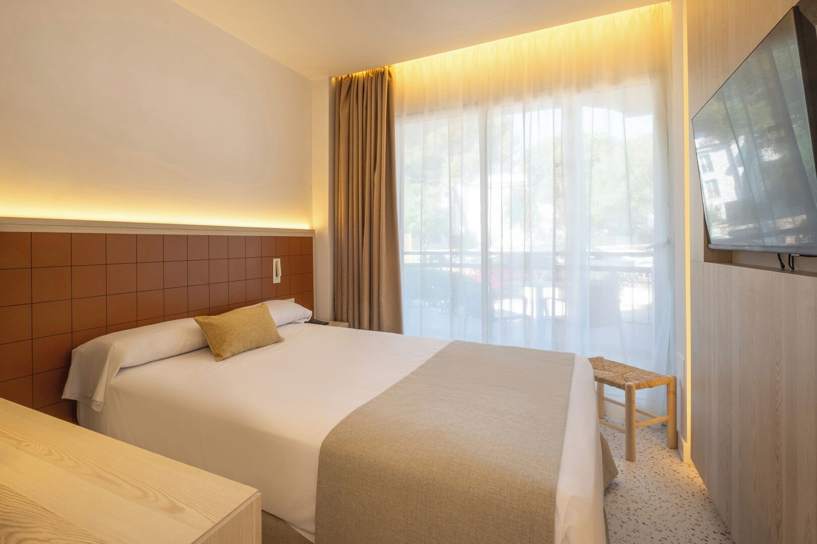 Une chambre d’hôtel avec un lit, une table de chevet en bois, une télévision et une fenêtre avec des rideaux.