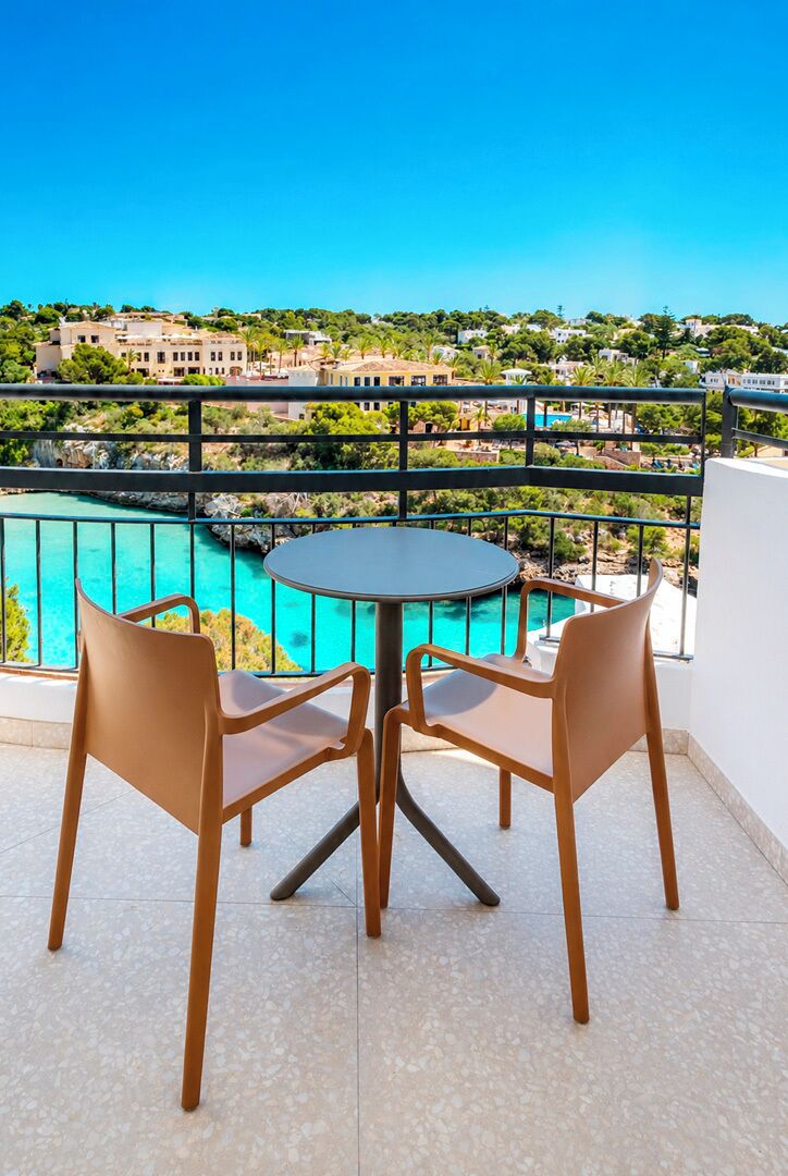 A balcony with a round table and four chairs, overlooking a turquoise pool and a hillside of buildings.