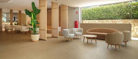Eine geräumige Lobby mit einer großen Pflanze in einem Topf, einer Sitzecke mit Sofas und Sesseln sowie einer Steinwand mit Bepflanzung.