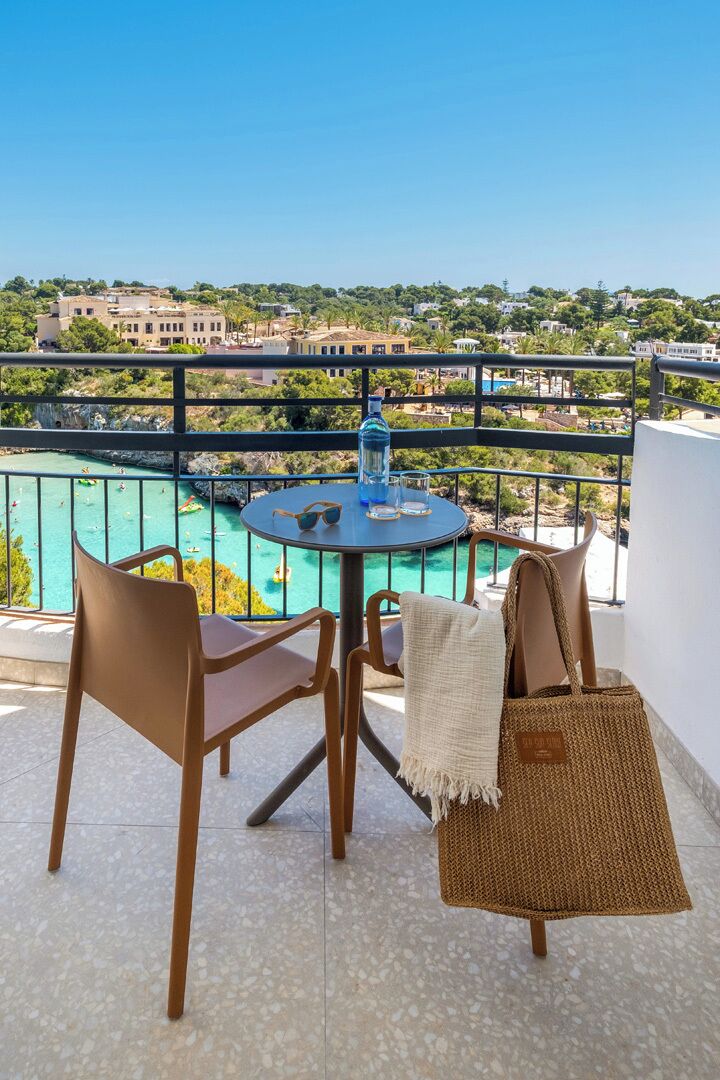 Een balkon met een tafel en stoelen, met uitzicht op een zwembad en een kustplaats.