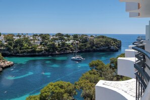 A coastal view with clear turquoise waters, boats, and a white building with balconies. -  Hotel Cabot Cala Ferrera (Felanitx)