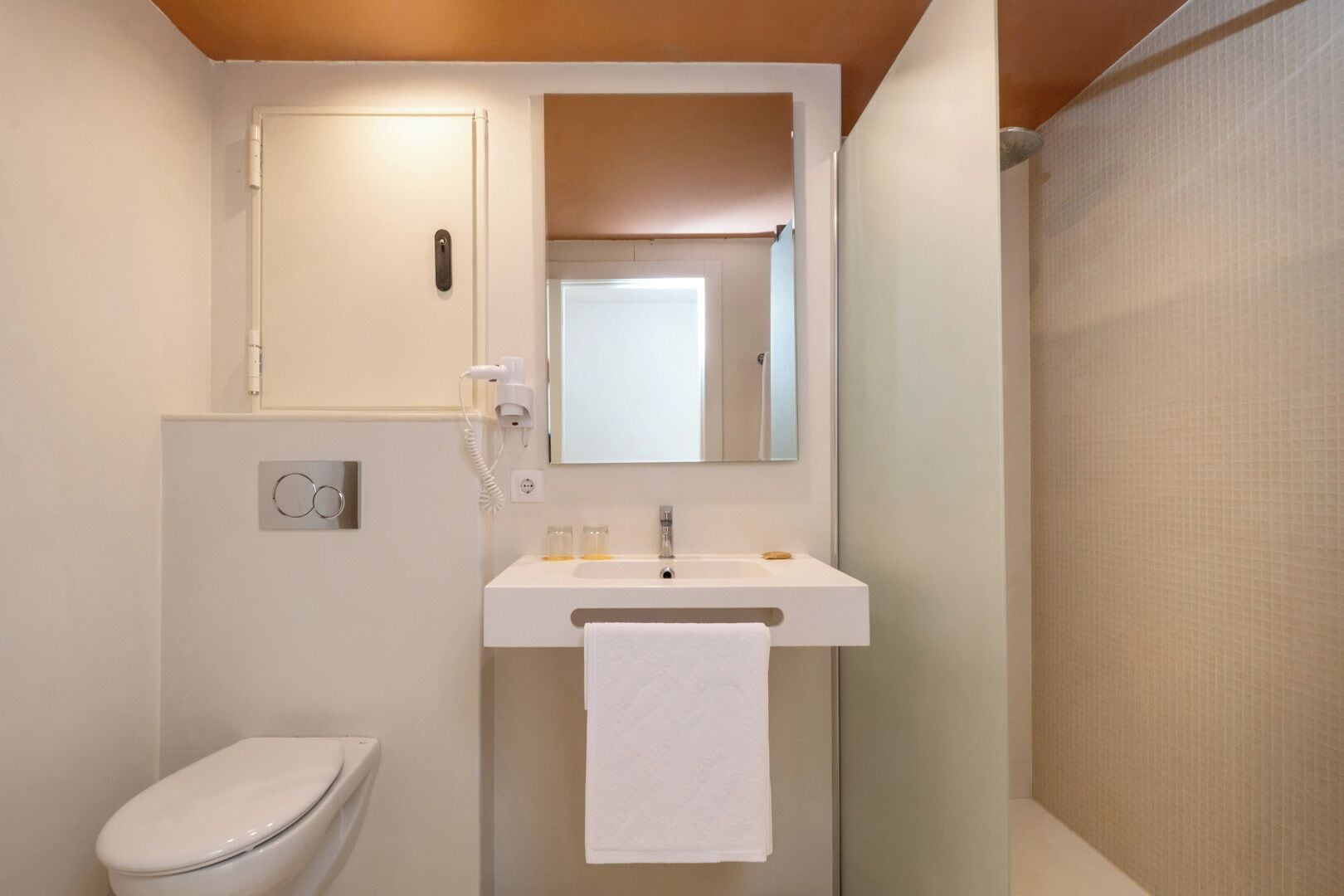 Un baño con inodoro, lavamanos con una toalla, espejo y cortina de ducha.