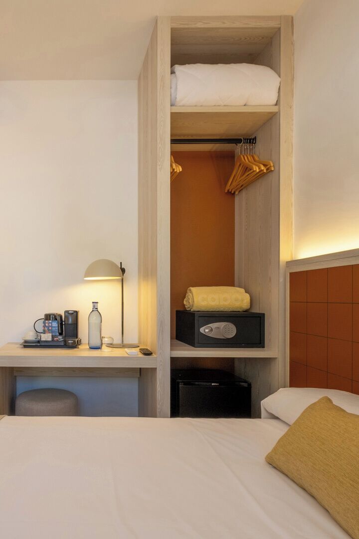 Une chambre d’hôtel équipée d’un lit, d’un bureau avec une lampe, d’une machine à café et d’une boîte de rangement.