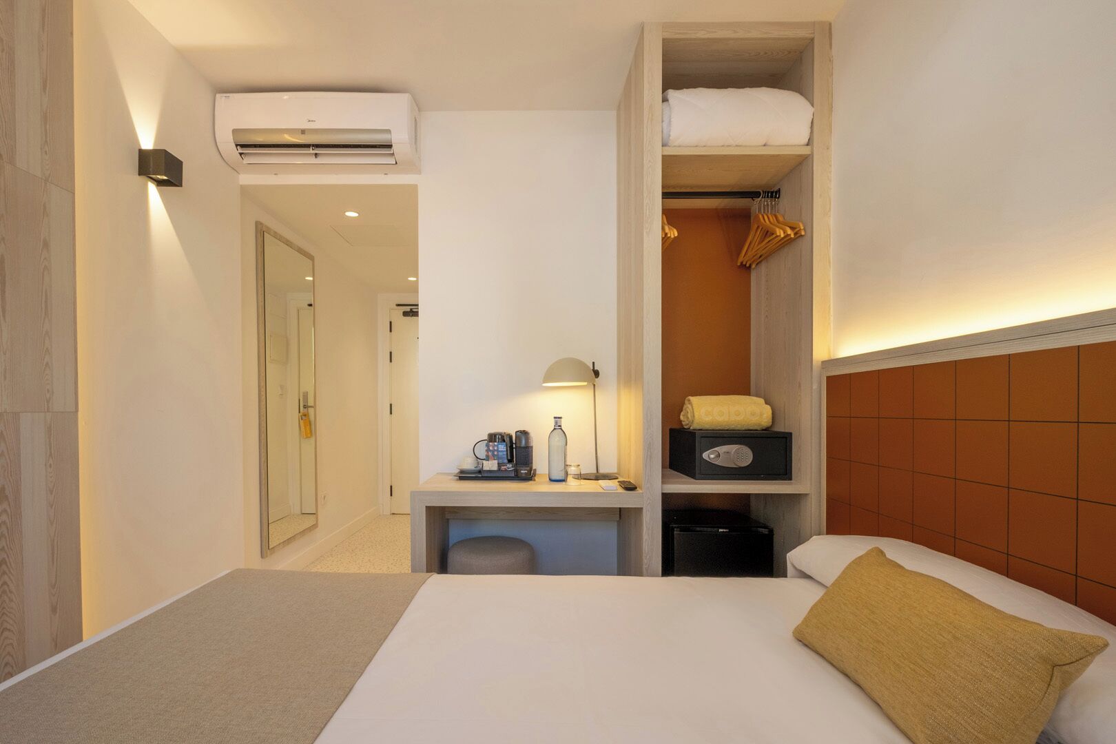 Ein Hotelzimmer mit Bett, Schreibtisch mit Lampe, Kleiderschrank und Klimaanlage.